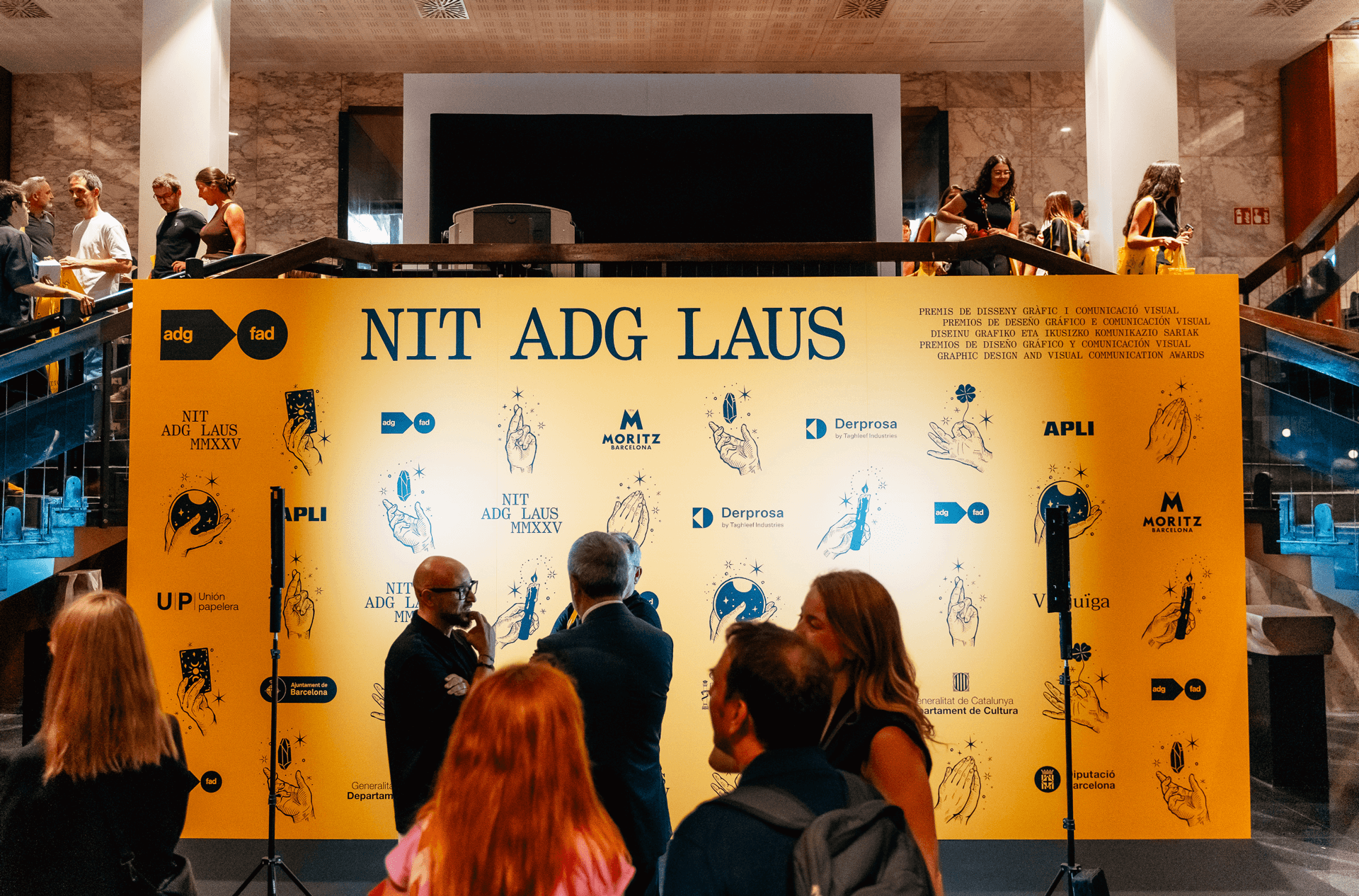 Fotocall de la Nit ADG Laus 2025 con gráfica de la campaña Rituales y asistentes al evento.